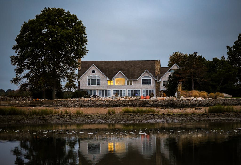 A picturesque waterfront home reflecting in calm water at twilight with warm interior lights.